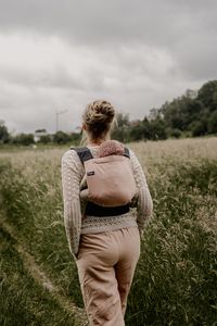 Jenny trägt Kind in Tragehilfe auf dem Rücken, spaziert durch die Natur